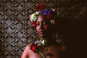 a woman standing against a textured background wearing a crown of flowers
